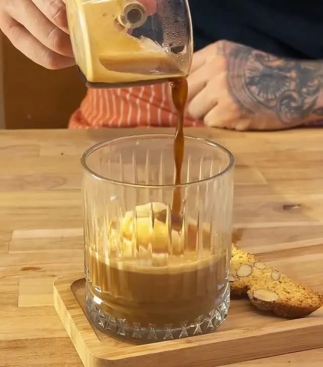 Café sendo derramado sobre o gelato no copo do affogato, com cantucci ao lado