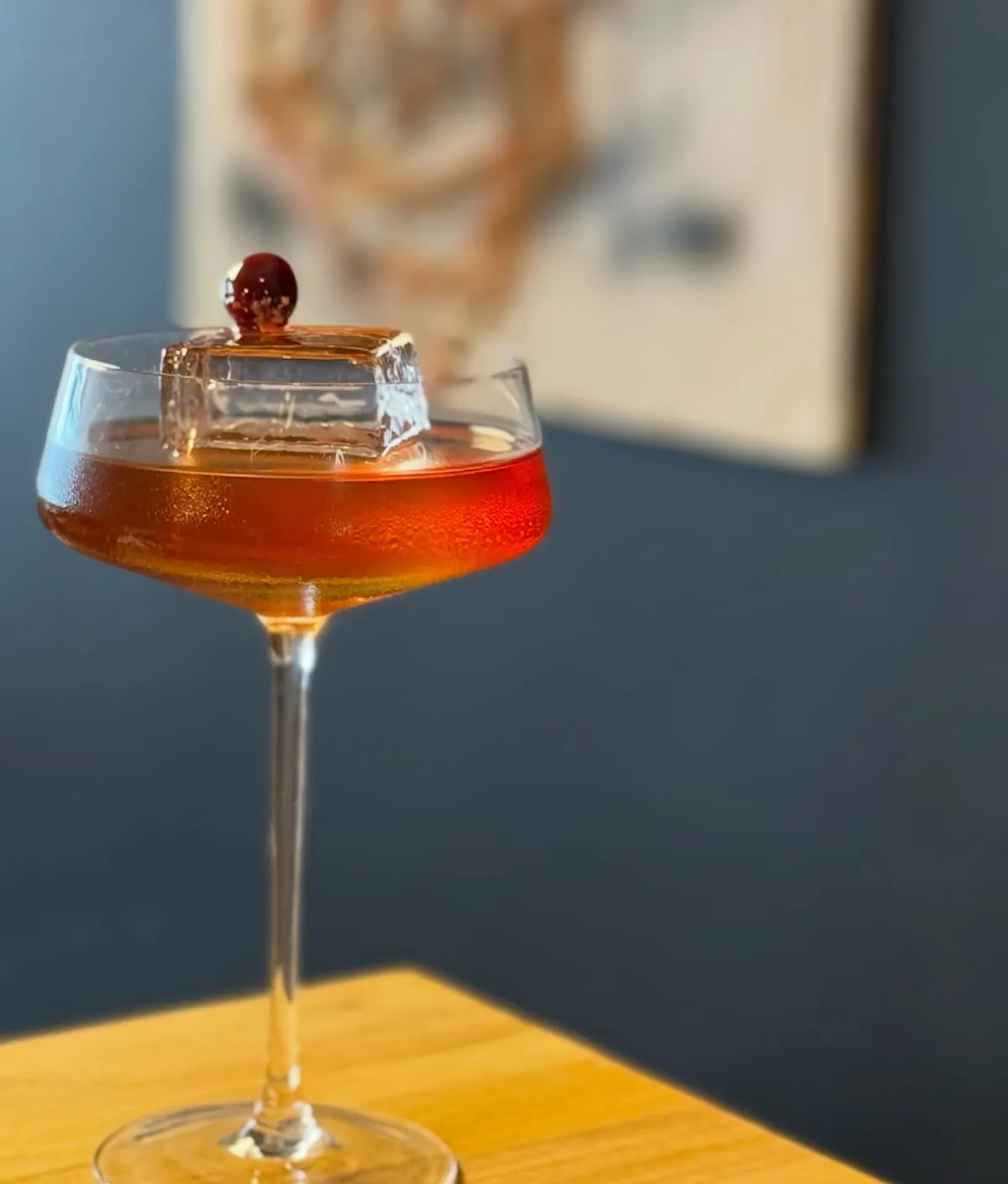 Drink âmbar numa taça, com a carta de drinks ao fundo