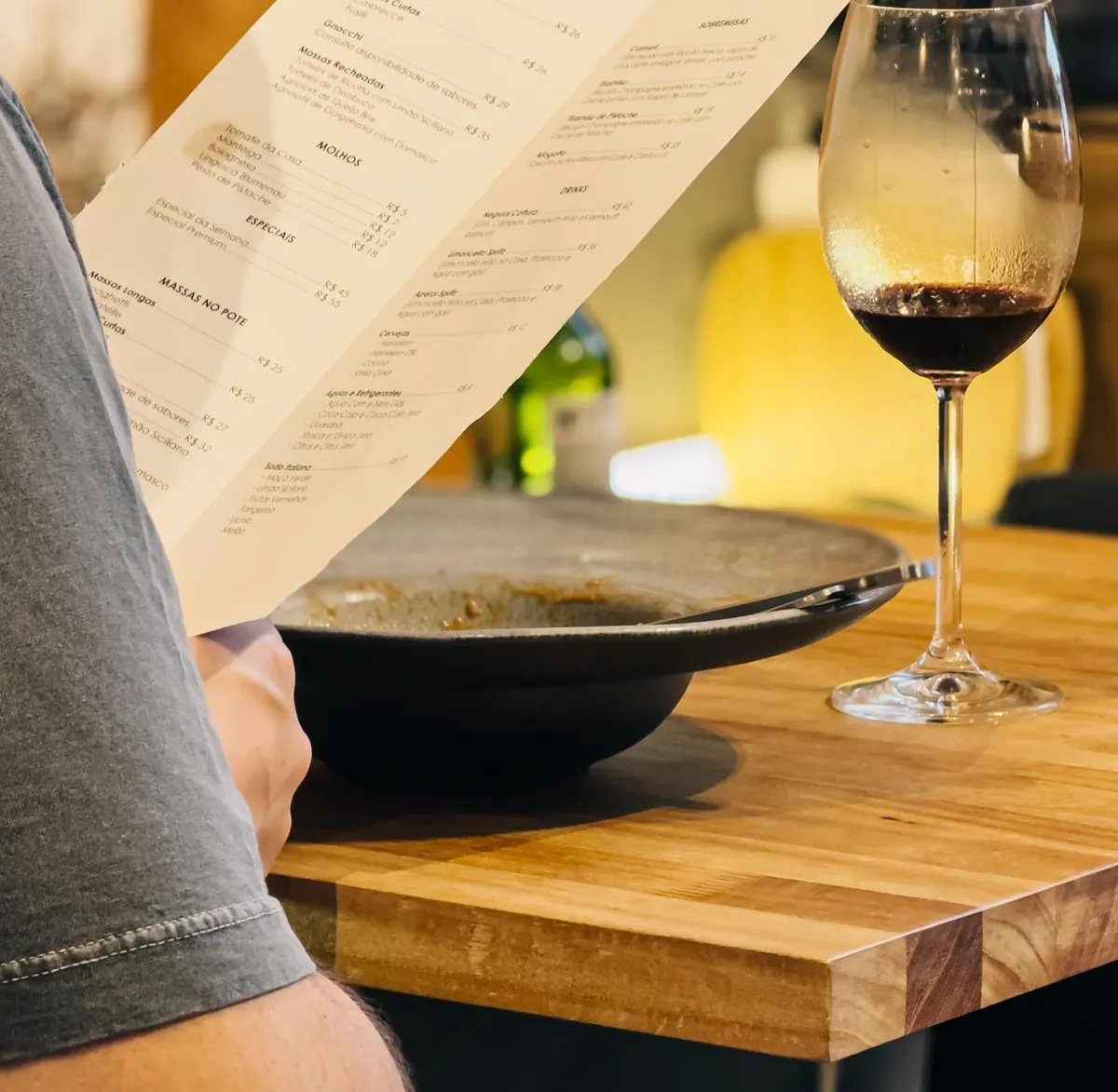 Taça de vinho tinto ao lado da carta, numa mesa do Cottura