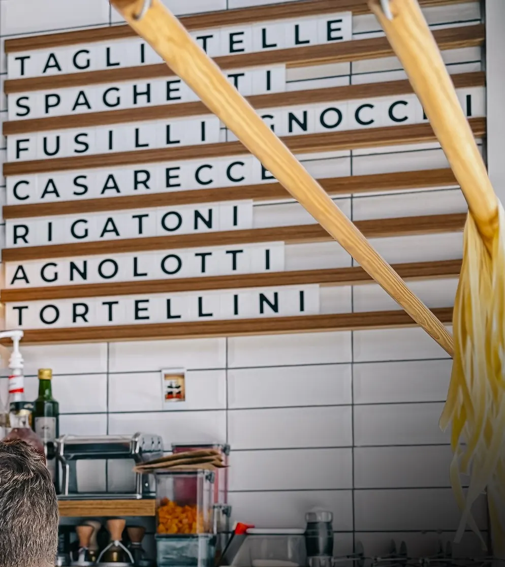 Quadro na parede com os nomes das massas: tagliatelle, spaghetti, fusilli, gnocchi, casarecce, rigatoni, agnolotti e tortellini